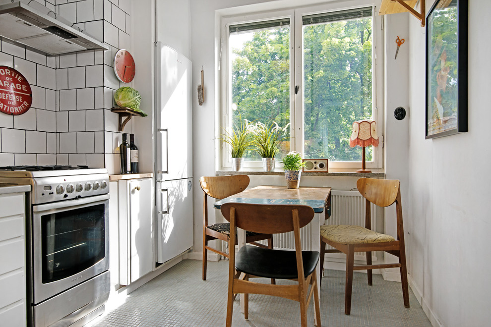 Eat-in kitchen - mid-sized scandinavian single-wall eat-in kitchen idea in Stockholm with white cabinets, white backsplash, subway tile backsplash, white appliances and flat-panel cabinets