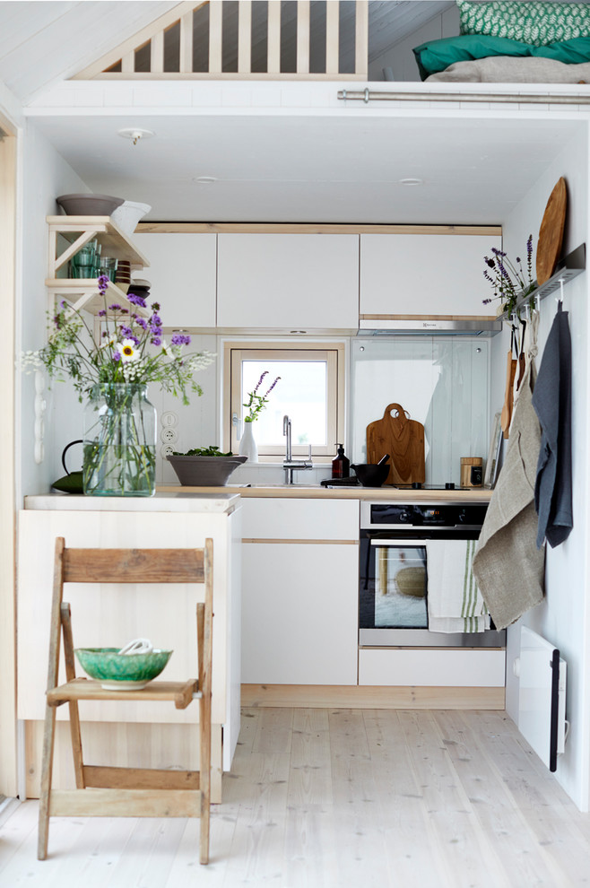 Example of a small danish single-wall light wood floor and beige floor kitchen design in Stockholm with flat-panel cabinets, white cabinets, a peninsula, a drop-in sink and beige countertops