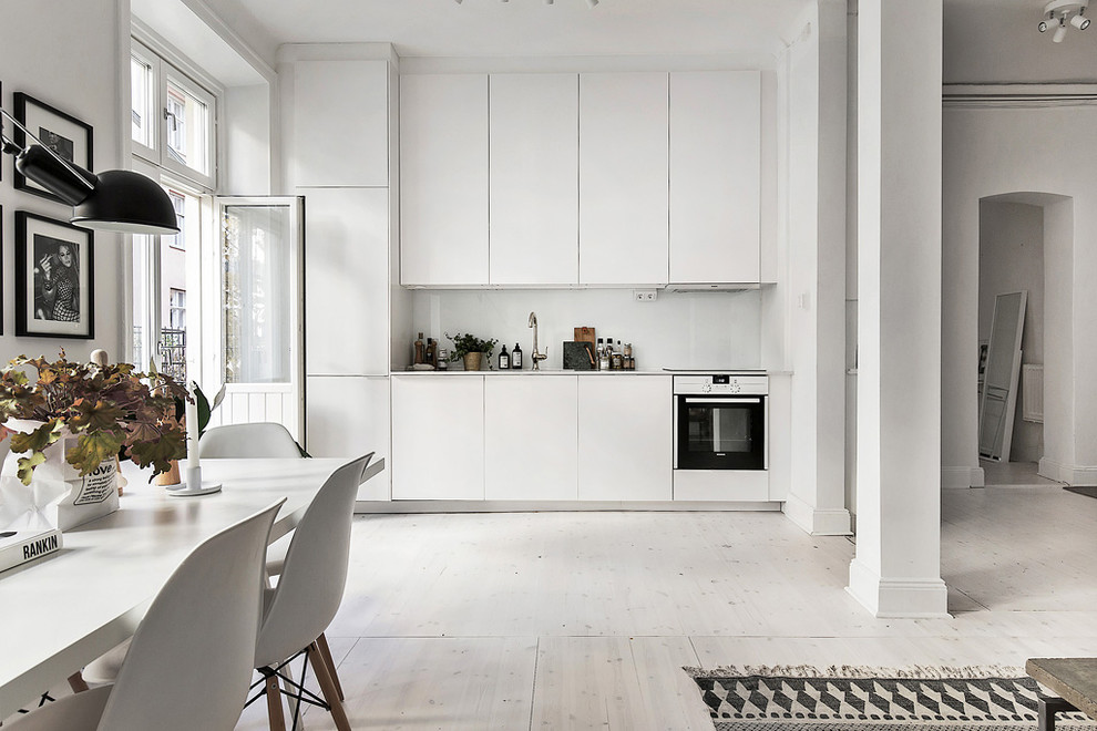 Einzeilige, Geräumige Wohnküche ohne Insel mit Doppelwaschbecken, flächenbündigen Schrankfronten, weißen Schränken, weißen Elektrogeräten und gebeiztem Holzboden in Stockholm