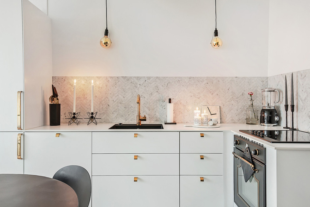 Photo of a medium sized scandinavian l-shaped open plan kitchen in Stockholm with a submerged sink, flat-panel cabinets, white cabinets, grey splashback, black appliances, no island, light hardwood flooring and laminate countertops.