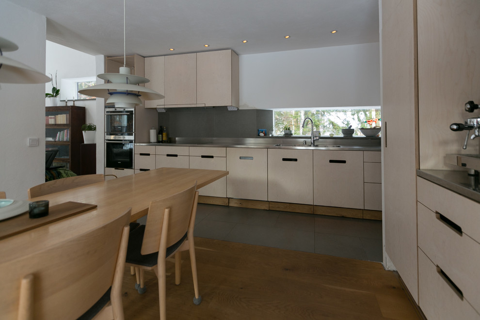 マルメにある広い北欧スタイルのおしゃれなキッチン (一体型シンク、ステンレスカウンター、グレーのキッチンパネル、セラミックタイルのキッチンパネル、シルバーの調理設備、セラミックタイルの床) の写真