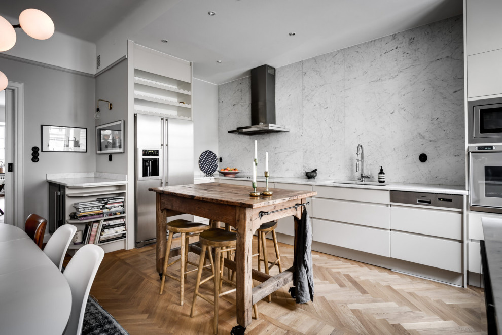 Aménagement d'une cuisine linéaire scandinave avec plan de travail en marbre, un électroménager en acier inoxydable, un sol en bois brun et îlot.