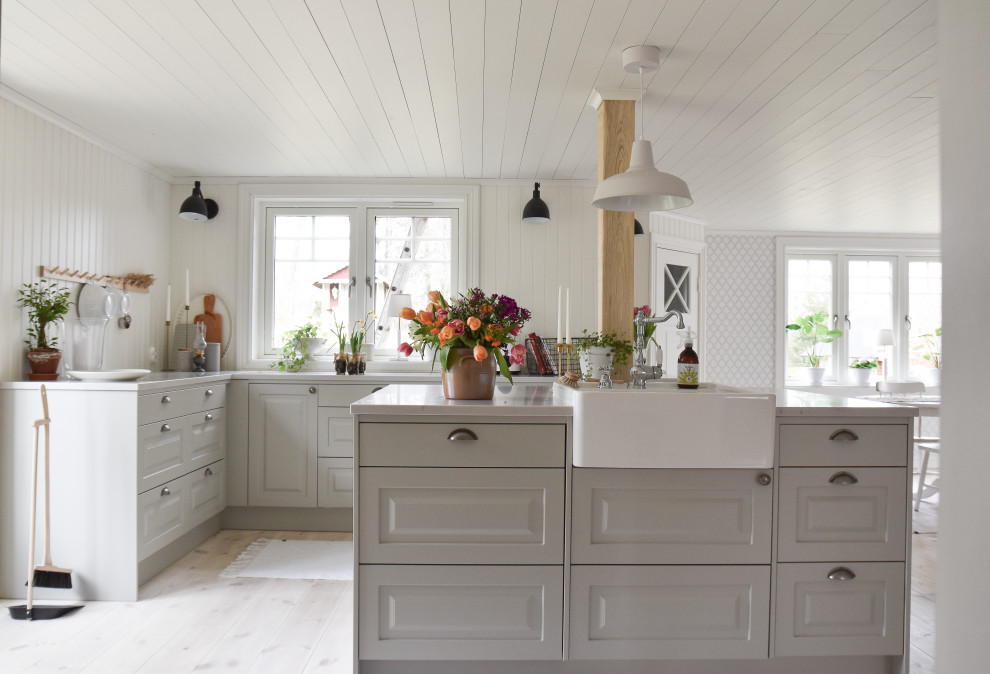 Cette photo montre une cuisine nature en L avec un évier de ferme, un placard avec porte à panneau surélevé, des portes de placard grises, parquet clair, îlot, un sol beige, un plan de travail blanc et un plafond en lambris de bois.