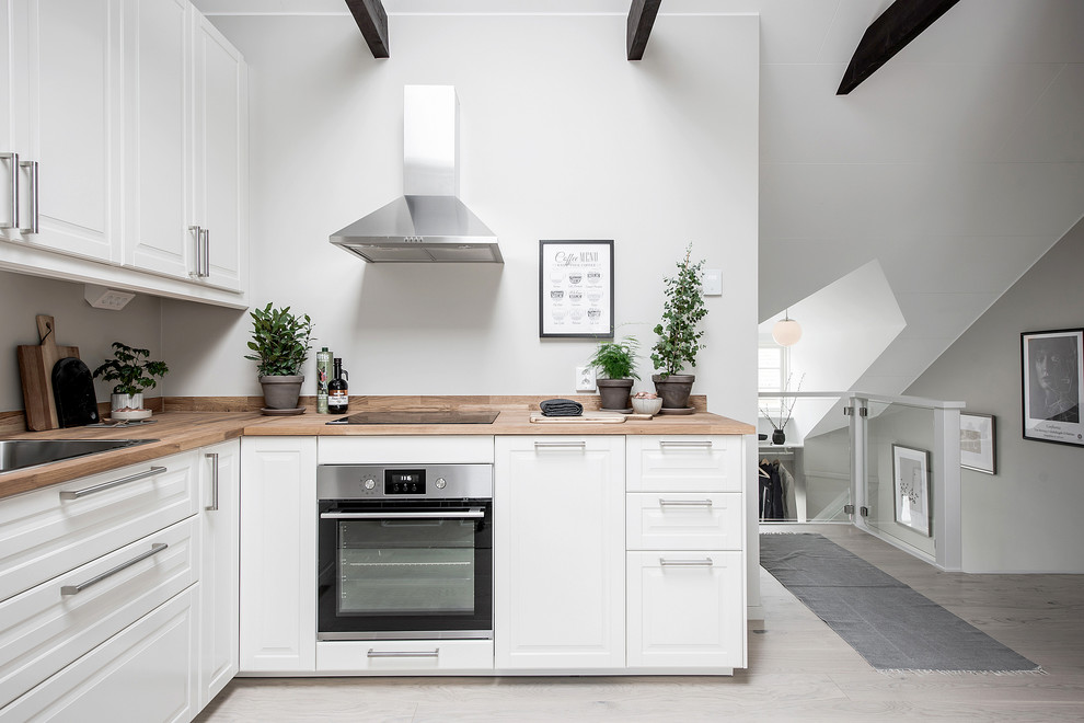Foto på ett litet nordiskt kök, med vita skåp, träbänkskiva, grått golv, en nedsänkt diskho, luckor med upphöjd panel, rostfria vitvaror och ljust trägolv