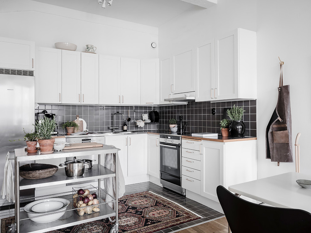 Foto på ett nordiskt flerfärgad kök, med skåp i shakerstil, vita skåp, svart stänkskydd, rostfria vitvaror, en köksö och svart golv