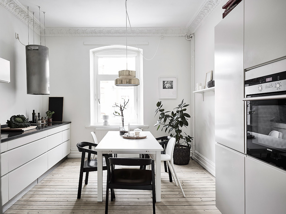Пример оригинального дизайна: прямая кухня среднего размера в скандинавском стиле с обеденным столом, плоскими фасадами, белыми фасадами, техникой из нержавеющей стали и светлым паркетным полом без острова