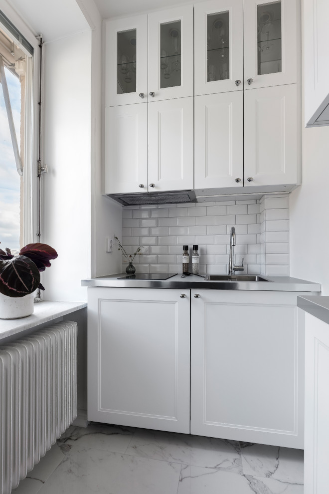 Foto på ett litet vintage grå l-kök, med en nedsänkt diskho, luckor med infälld panel, vita skåp, bänkskiva i rostfritt stål, vitt stänkskydd, stänkskydd i tunnelbanekakel, rostfria vitvaror och grått golv