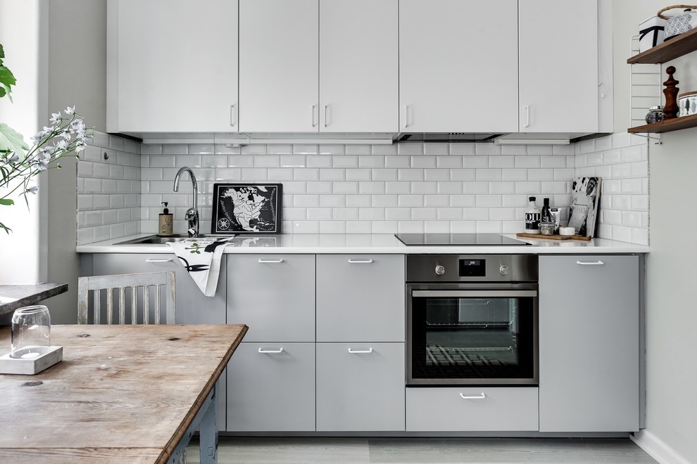 Kleine Klassische Küche in L-Form mit Waschbecken, flächenbündigen Schrankfronten, grauen Schränken, Küchenrückwand in Weiß, Küchengeräten aus Edelstahl, hellem Holzboden und Kücheninsel in Stockholm