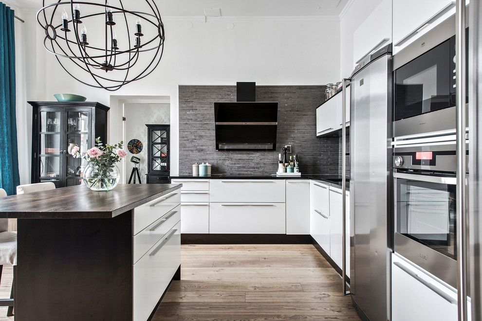 Foto på ett funkis kök, med släta luckor, vita skåp, träbänkskiva, grått stänkskydd, stänkskydd i stickkakel, rostfria vitvaror, en köksö och brunt golv