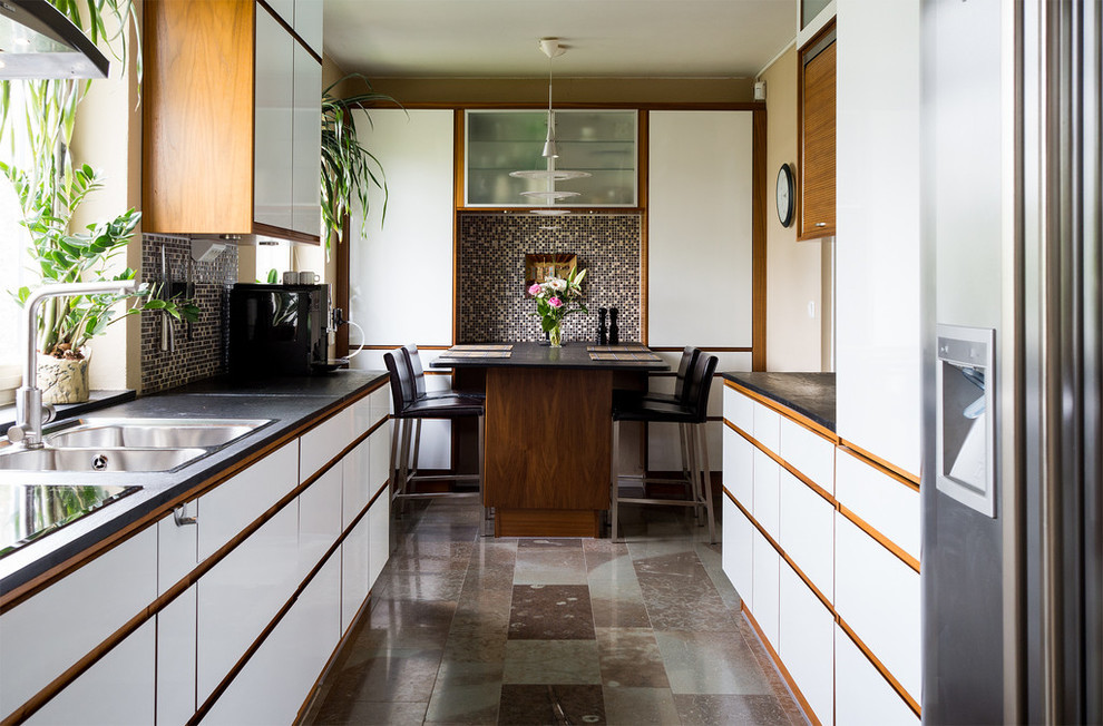 ストックホルムにある高級な中くらいなミッドセンチュリースタイルのおしゃれなキッチン (フラットパネル扉のキャビネット、白いキャビネット、御影石カウンター、シルバーの調理設備、アイランドなし) の写真