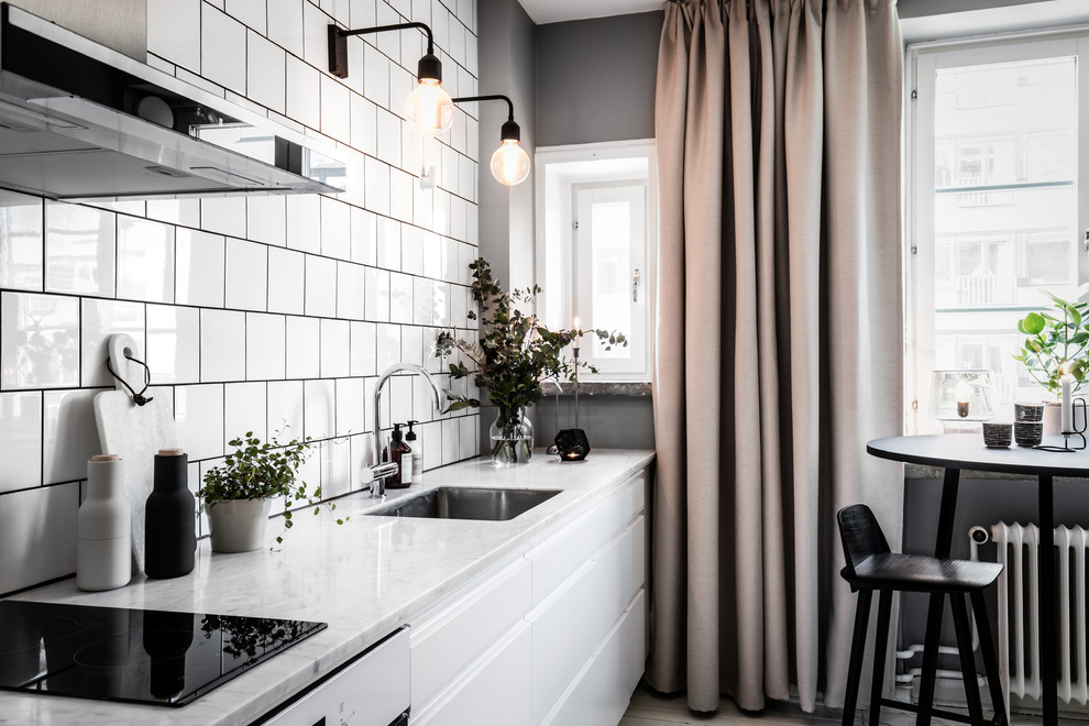 Bild på ett litet minimalistiskt linjärt kök med öppen planlösning, med vita skåp, marmorbänkskiva, vitt stänkskydd, stänkskydd i keramik och rostfria vitvaror