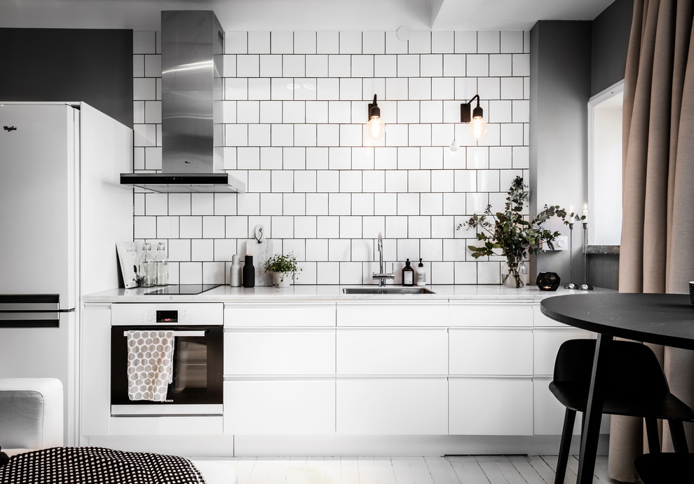 ヨーテボリにある小さな北欧スタイルのおしゃれなキッチン (白いキャビネット、大理石カウンター、白いキッチンパネル、セラミックタイルのキッチンパネル、白い調理設備、塗装フローリング、アイランドなし、白い床) の写真