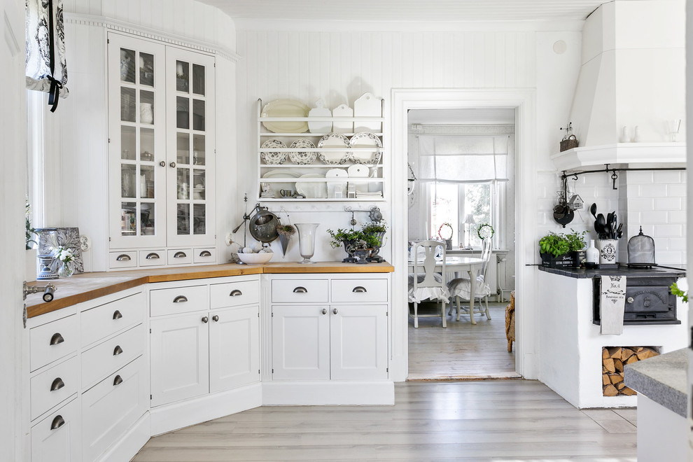 Inspiration for a shabby-chic style beige floor enclosed kitchen remodel in Other with glass-front cabinets, white cabinets, wood countertops, white backsplash and subway tile backsplash