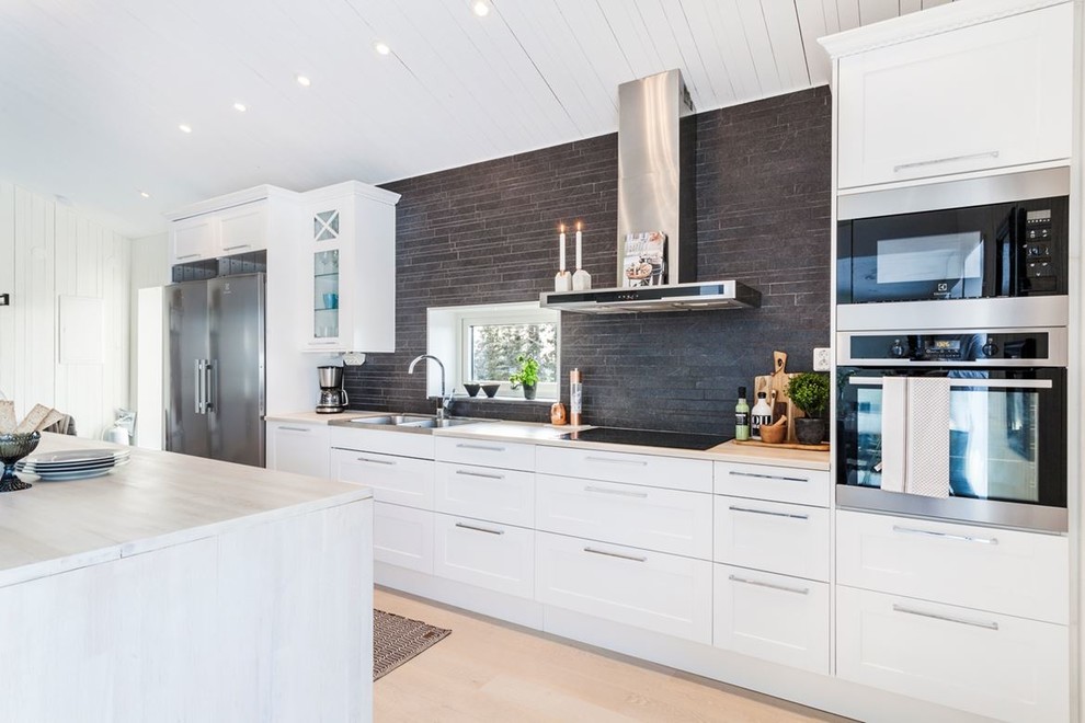 Exempel på ett minimalistiskt kök, med skåp i shakerstil, vita skåp, svart stänkskydd, en köksö, en dubbel diskho, rostfria vitvaror, ljust trägolv och beiget golv