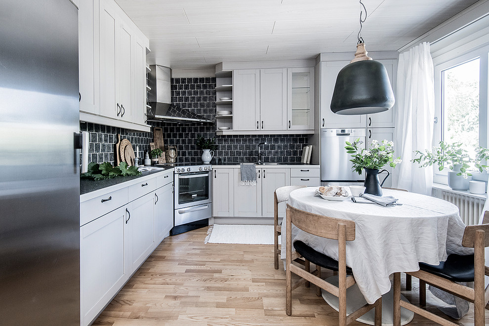Bild på ett mellanstort minimalistiskt grå grått kök, med vita skåp, svart stänkskydd, ljust trägolv, beiget golv, en dubbel diskho, skåp i shakerstil, stänkskydd i tunnelbanekakel och rostfria vitvaror