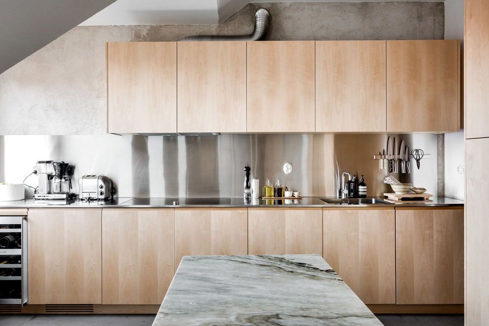 Bild på ett stort funkis linjärt kök, med släta luckor, skåp i ljust trä, bänkskiva i rostfritt stål, stänkskydd med metallisk yta, rostfria vitvaror och betonggolv