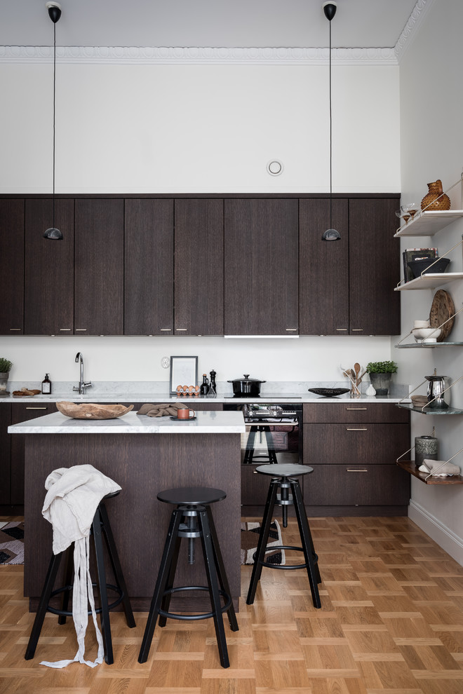 This is an example of a scandi kitchen in Gothenburg with flat-panel cabinets, dark wood cabinets, black appliances, light hardwood flooring, an island and white worktops.