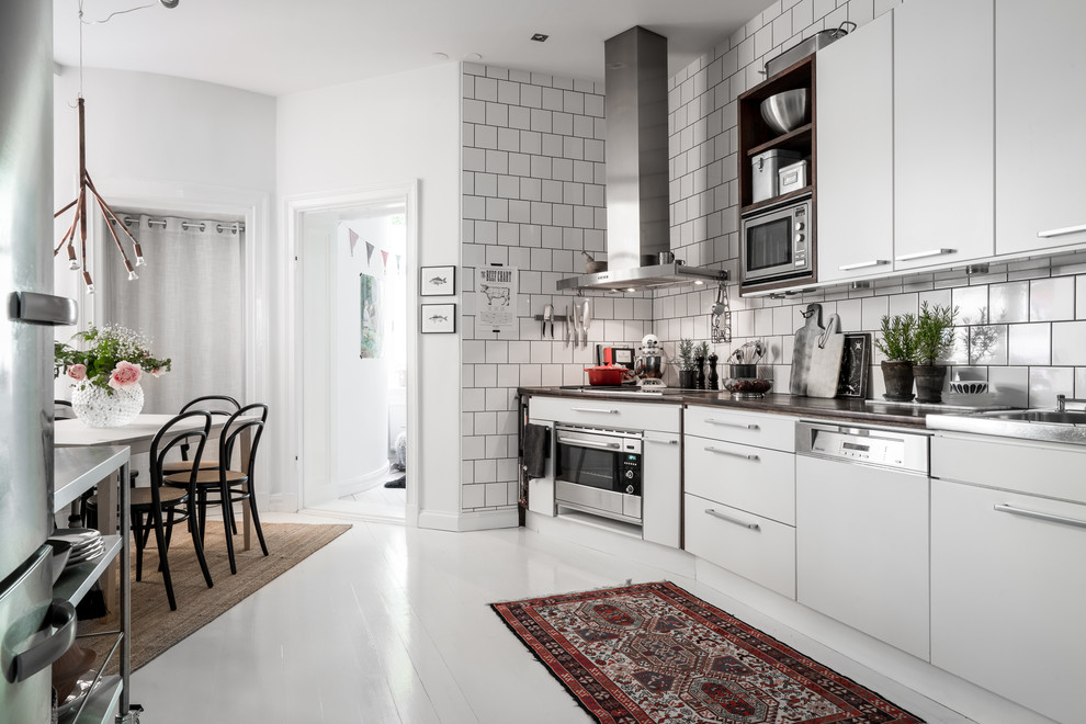 Skandinavisk inredning av ett mellanstort linjärt kök och matrum, med släta luckor, vita skåp, bänkskiva i rostfritt stål, stänkskydd i porslinskakel och rostfria vitvaror