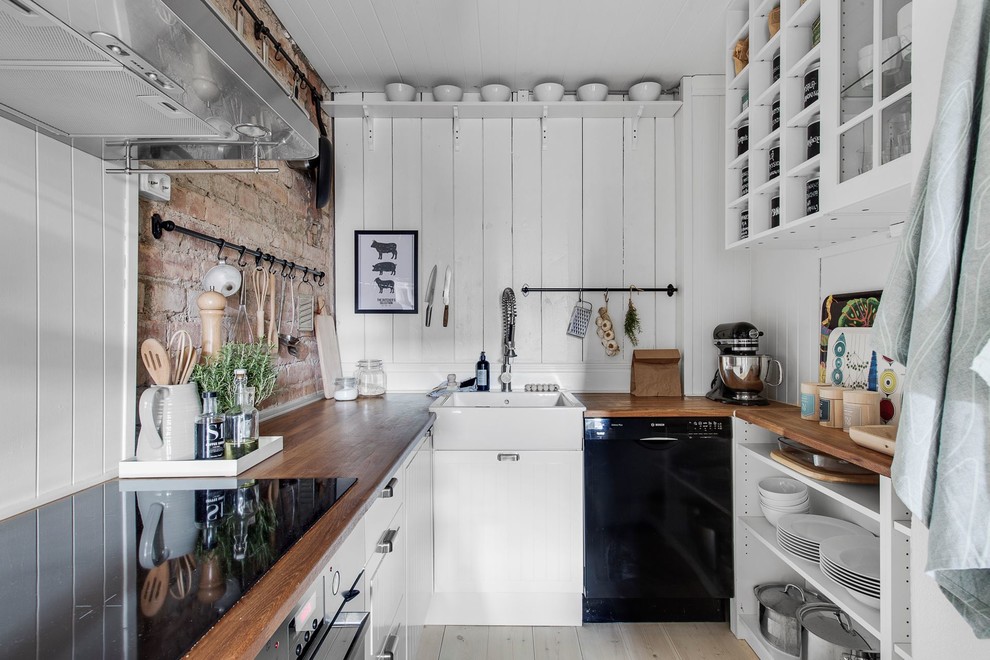 Foto på ett litet lantligt u-kök, med en enkel diskho, öppna hyllor, vita skåp, träbänkskiva, vitt stänkskydd, stänkskydd i trä, svarta vitvaror och ljust trägolv