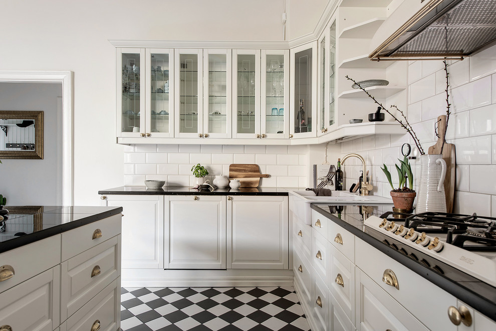 Foto på ett nordiskt kök, med en rustik diskho, luckor med upphöjd panel, vitt stänkskydd, stänkskydd i tunnelbanekakel, integrerade vitvaror, en köksö och flerfärgat golv