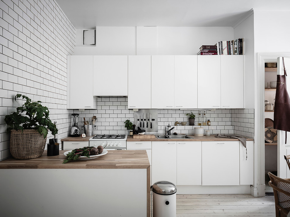 Exempel på ett mellanstort skandinaviskt beige linjärt beige kök och matrum, med släta luckor, vita skåp, vitt stänkskydd, en halv köksö, en dubbel diskho, träbänkskiva, stänkskydd i tunnelbanekakel, vita vitvaror, målat trägolv och vitt golv