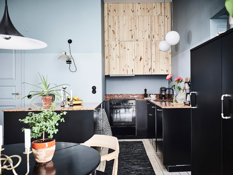 Modelo de cocina comedor nórdica grande sin isla con armarios con paneles lisos, puertas de armario negras, electrodomésticos negros y suelo de madera pintada