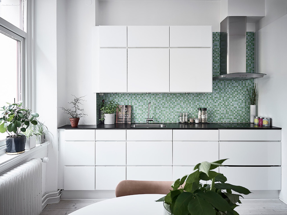 Пример оригинального дизайна: кухня в скандинавском стиле с врезной мойкой, плоскими фасадами, белыми фасадами, зеленым фартуком, светлым паркетным полом и серым полом
