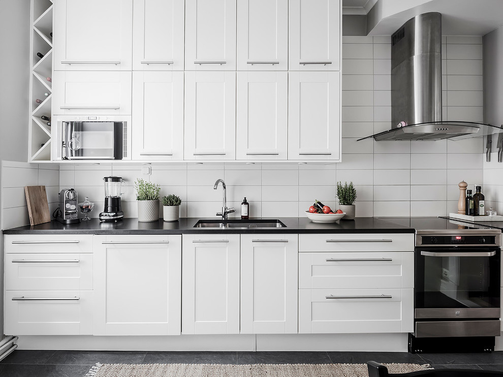 Ejemplo de cocina lineal nórdica de tamaño medio con armarios con paneles empotrados, puertas de armario blancas y encimeras negras