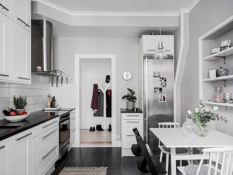 Diseño de cocina lineal nórdica sin isla con armarios con paneles empotrados, puertas de armario blancas, electrodomésticos de acero inoxidable y suelo negro