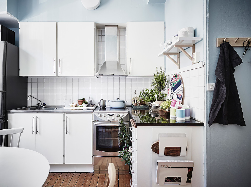 Inspiration för ett litet nordiskt kök, med släta luckor, vita skåp, bänkskiva i rostfritt stål, vitt stänkskydd, en dubbel diskho, rostfria vitvaror, mellanmörkt trägolv och brunt golv