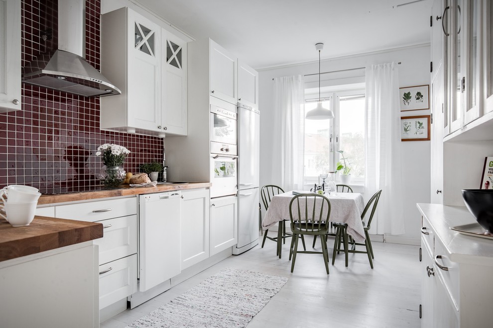 Idéer för ett skandinaviskt kök, med en nedsänkt diskho, luckor med infälld panel, vita skåp, träbänkskiva, rött stänkskydd, stänkskydd i mosaik, vita vitvaror, målat trägolv och vitt golv