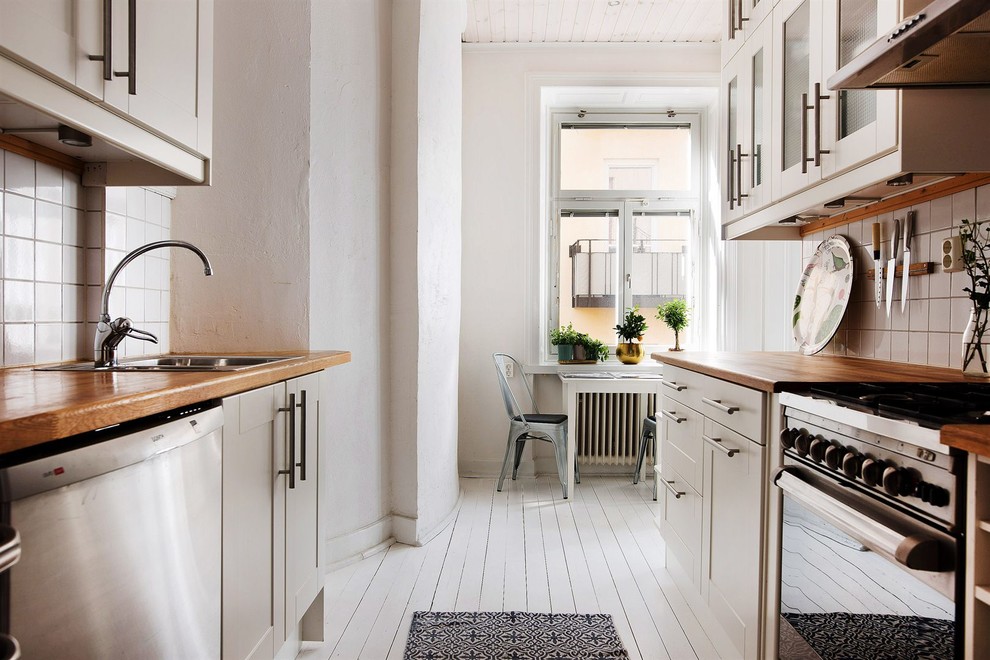 Photo of a medium sized scandinavian galley kitchen/diner in Stockholm with a built-in sink, shaker cabinets, white cabinets, wood worktops, white splashback, stainless steel appliances, painted wood flooring and no island.