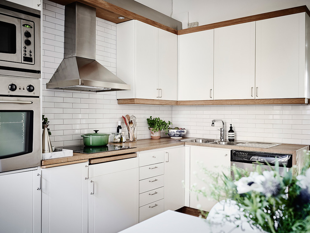 Inredning av ett nordiskt mellanstort kök, med en dubbel diskho, luckor med profilerade fronter, vita skåp, träbänkskiva, vitt stänkskydd, stänkskydd i tunnelbanekakel, mellanmörkt trägolv och rostfria vitvaror