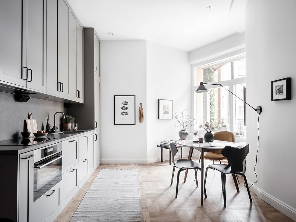 Foto på ett mellanstort nordiskt grå linjärt kök och matrum, med luckor med infälld panel, grå skåp, grått stänkskydd, en undermonterad diskho, integrerade vitvaror, mellanmörkt trägolv och beiget golv