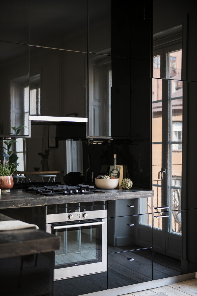 Пример оригинального дизайна: маленькая отдельная, угловая кухня в скандинавском стиле с плоскими фасадами, черными фасадами, черным фартуком, техникой под мебельный фасад, светлым паркетным полом, бежевым полом и коричневой столешницей для на участке и в саду