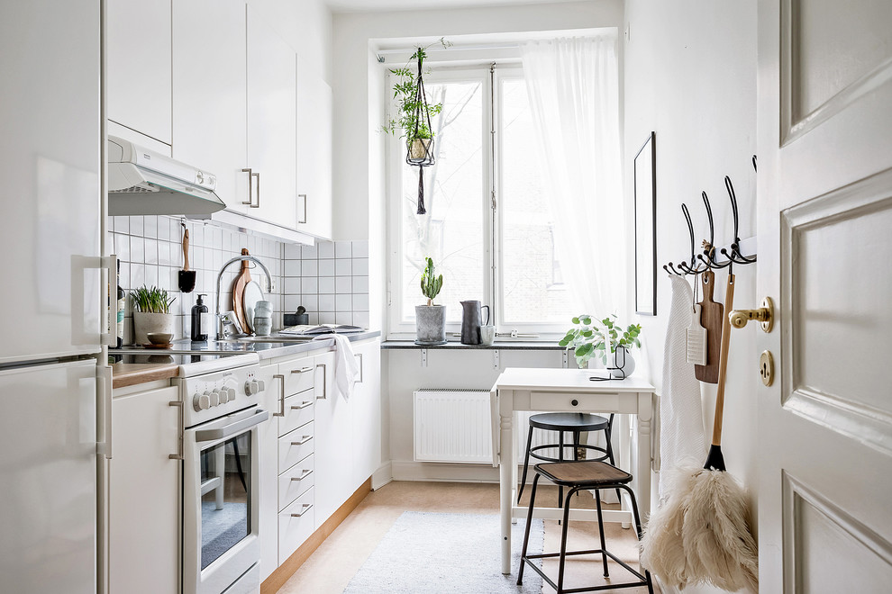 Photo of a small scandi single-wall kitchen/diner in Gothenburg with flat-panel cabinets, white cabinets, stainless steel worktops, white splashback, lino flooring, no island and beige floors.