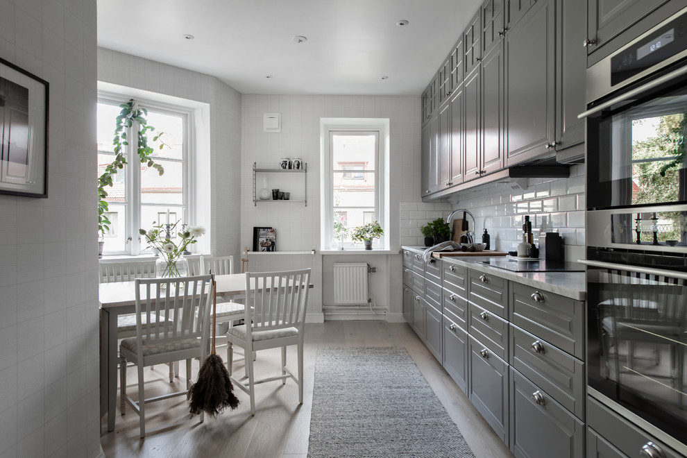 Idéer för ett skandinaviskt vit linjärt kök och matrum, med luckor med upphöjd panel, grå skåp, marmorbänkskiva, vitt stänkskydd, stänkskydd i tunnelbanekakel, integrerade vitvaror, ljust trägolv och beiget golv