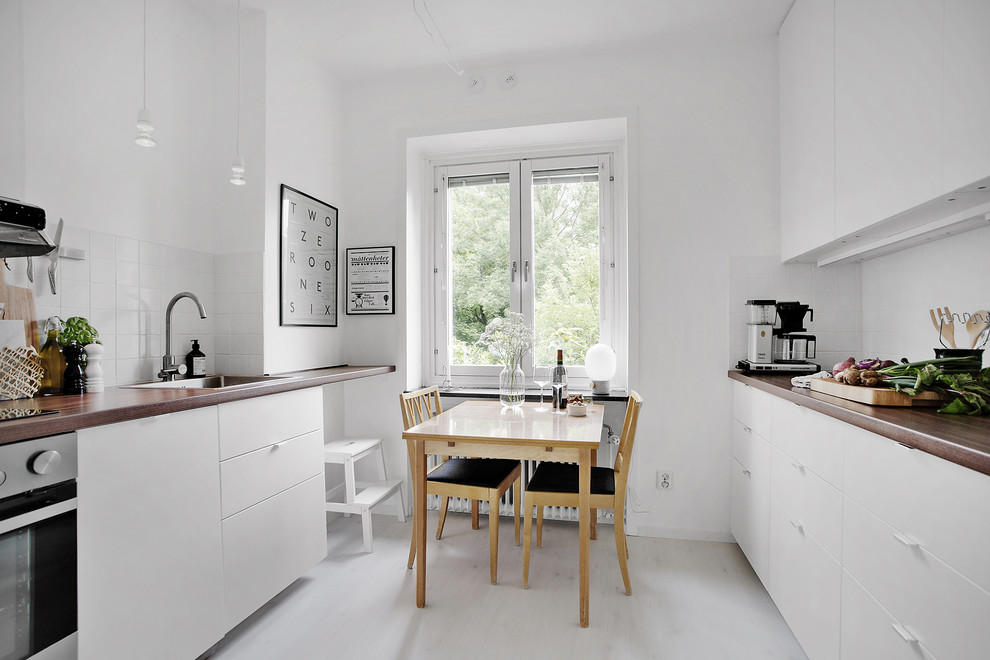 Idéer för att renovera ett minimalistiskt kök, med en nedsänkt diskho, släta luckor, vita skåp, träbänkskiva, vitt stänkskydd, stänkskydd i tunnelbanekakel, rostfria vitvaror, ljust trägolv och vitt golv