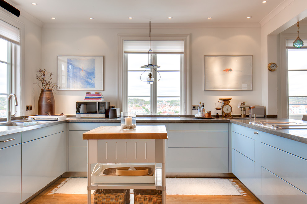 Idéer för mellanstora skandinaviska u-kök, med en dubbel diskho, släta luckor, blå skåp, granitbänkskiva, ljust trägolv och en köksö