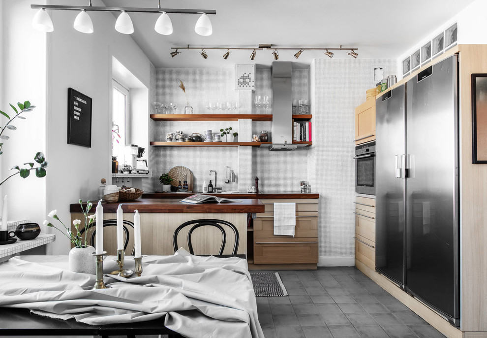This is an example of a medium sized scandi l-shaped kitchen/diner in Stockholm with light wood cabinets, grey splashback, mosaic tiled splashback, a breakfast bar, grey floors, shaker cabinets, wood worktops, stainless steel appliances and brown worktops.