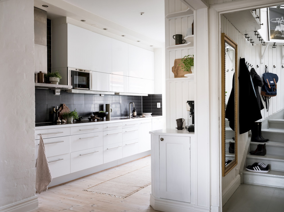 Cette photo montre une cuisine parallèle scandinave avec un placard à porte plane, des portes de placard blanches, une crédence noire, parquet clair, aucun îlot, un sol beige et un plan de travail blanc.