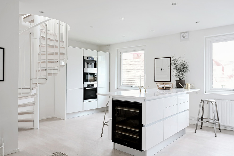 Inredning av ett skandinaviskt mellanstort linjärt kök med öppen planlösning, med släta luckor, vita skåp, svarta vitvaror, ljust trägolv, en köksö och vitt golv
