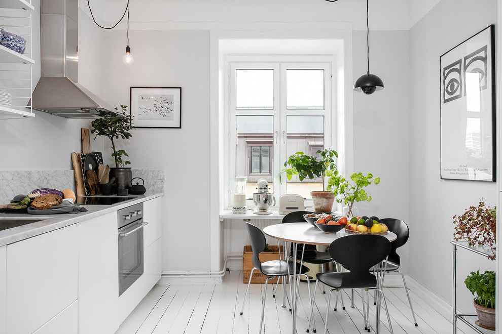 На фото: прямая кухня в скандинавском стиле с обеденным столом, врезной мойкой, плоскими фасадами, белыми фасадами, белым фартуком, техникой из нержавеющей стали, деревянным полом, белым полом и окном без острова с