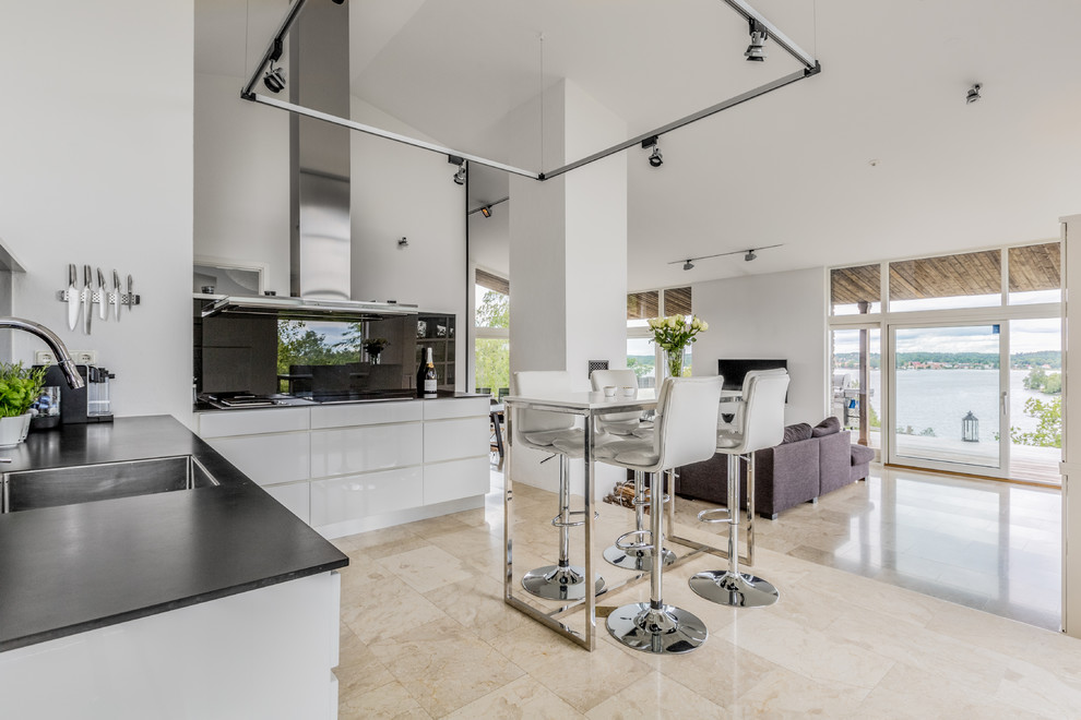 Modern inredning av ett kök, med en enkel diskho, släta luckor, vita skåp, bänkskiva i onyx, vitt stänkskydd, glaspanel som stänkskydd och beiget golv
