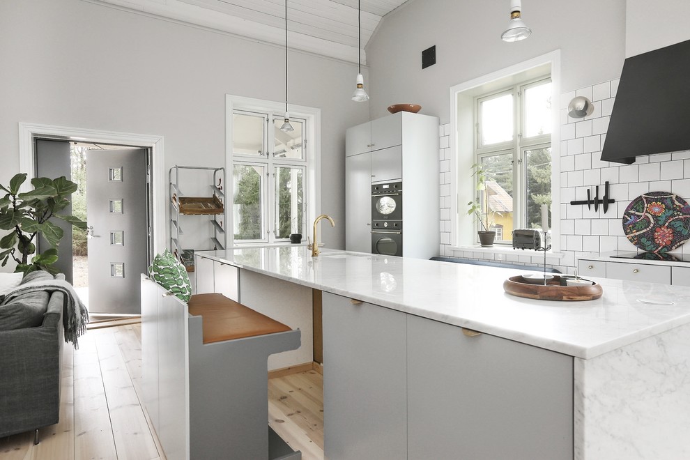 Inredning av ett nordiskt kök med öppen planlösning, med en undermonterad diskho, släta luckor, grå skåp, vitt stänkskydd, ljust trägolv, en köksö och beiget golv