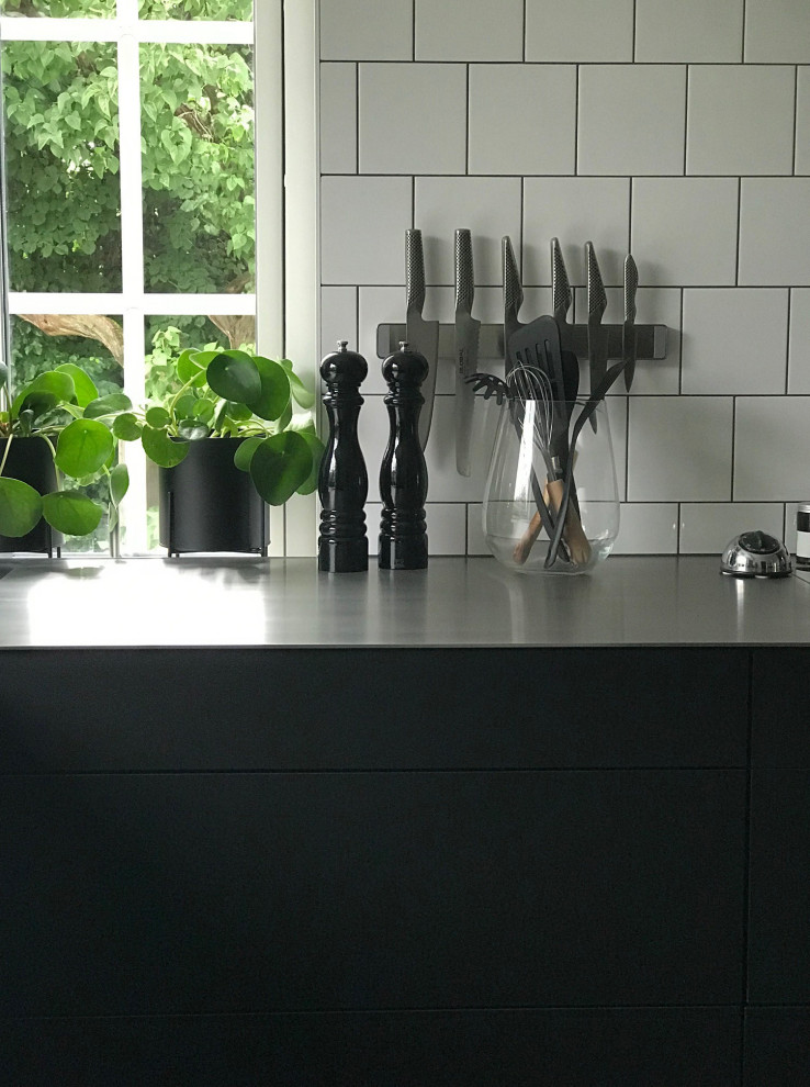 Inspiration för ett nordiskt svart svart kök och matrum, med en undermonterad diskho, släta luckor, svarta skåp, bänkskiva i rostfritt stål, rostfria vitvaror och klinkergolv i keramik