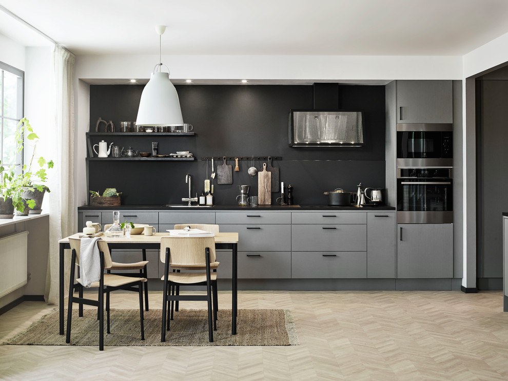 Example of a danish single-wall light wood floor and beige floor eat-in kitchen design in Gothenburg with an undermount sink, flat-panel cabinets, gray cabinets, black backsplash, paneled appliances, no island and black countertops