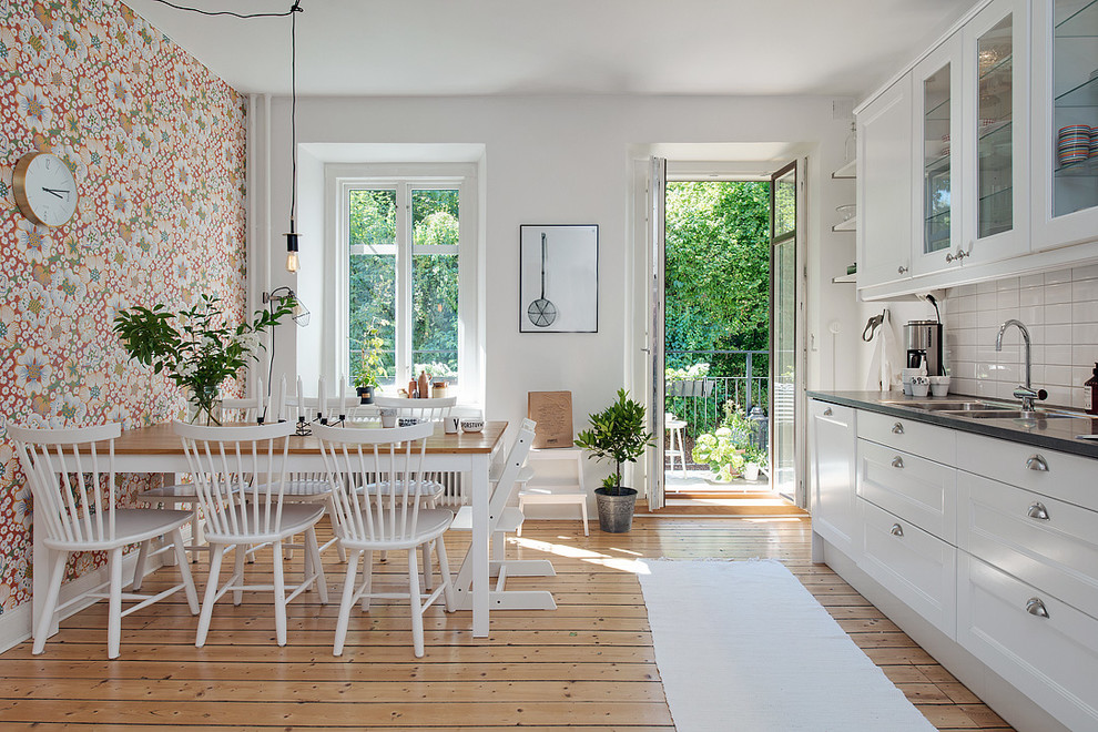 Immagine di una cucina scandinava di medie dimensioni con lavello a doppia vasca, ante di vetro, ante bianche, paraspruzzi bianco, pavimento in legno massello medio, nessuna isola e top in acciaio inossidabile