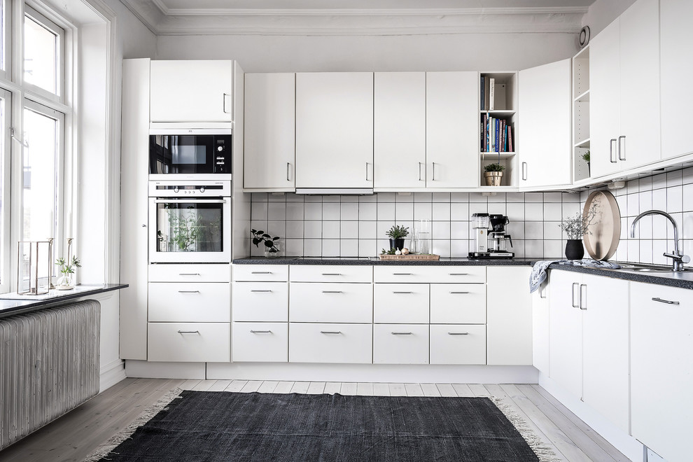 Skandinavische Küche ohne Insel in L-Form mit Einbauwaschbecken, flächenbündigen Schrankfronten, Küchenrückwand in Weiß, Küchengeräten aus Edelstahl und hellem Holzboden in Göteborg