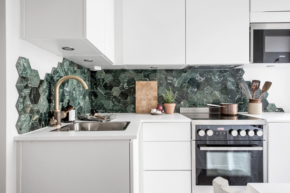 Inspiration för små moderna l-kök, med en nedsänkt diskho, släta luckor, vita skåp, grönt stänkskydd, stänkskydd i mosaik och rostfria vitvaror